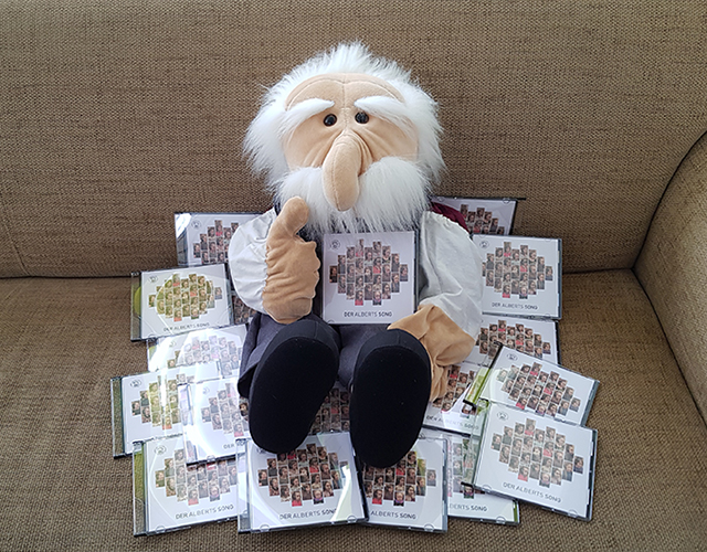 Maskottchen Albert umgeben von CDs des Chors "Albertinies"